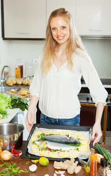 Positive housewife cooking full fish with potato  - Photo, image