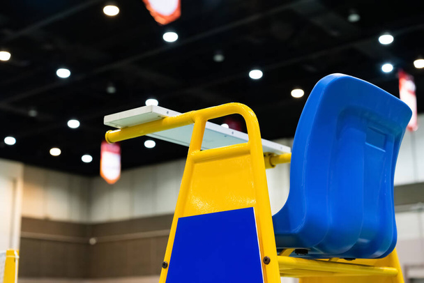 Синій стілець бадмінтону арбітр з жовтими кольорами біля бадмінтону сітки з розмитим фоном на спортивному стадіоні
. - Фото, зображення