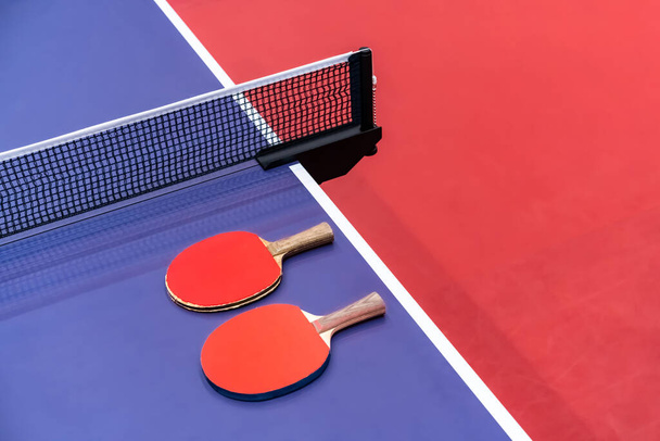 Two pingpong table tennis rackets for playing are laid on next to net on the blue table. This is one of ping pong sports equipment for players - Valokuva, kuva
