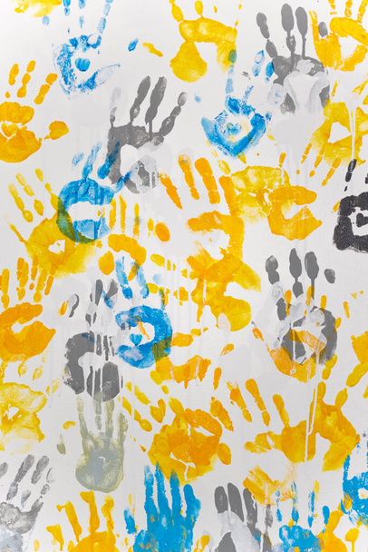 bright prints of children's hands from paint on the wall, yellow, blue, gray, vertical format - Foto, Imagen