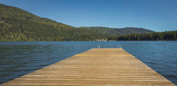 Wooden pier with metal ladder into the sea, lake, water. Swimming dock pier with metal ladder on calm blue lake at sunny day on idyllic resort at Cultus Lake BC - Photo, image