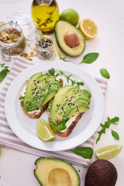 Freshly made Avocado and cream cheese toasts on a white ceramic plate and ingredients. - Φωτογραφία, εικόνα
