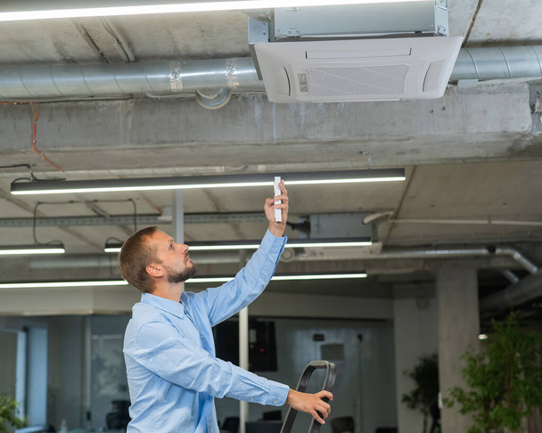 Caucasian bearded man repairing the air conditioner in the office - Fotó, kép
