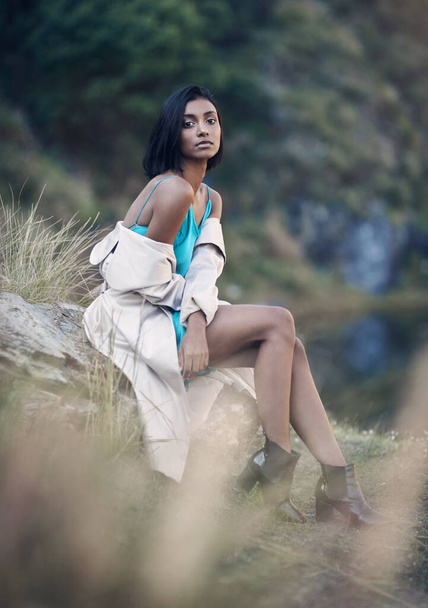 То, как ты одеваешься, выражает твою уверенность. модная молодая женщина, сидящая на скале на открытом воздухе - Фото, изображение