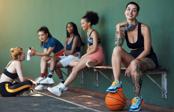 Chilling after another victory. Full length portrait of an attractive young female athlete sitting on a bench at the basketball court with her teammates in the background - Foto, immagini