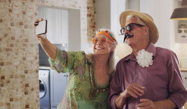 Say cheese. a happy senior couple standing together in costume and using a cellphone to take selfies - Photo, Image