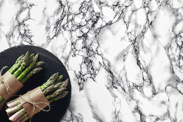 Bunch of an edible, juicy stalks of asparagus on a stone slate, marble background. Fresh, green vegetables, top view. Healthy meal. Spring harvest, agricultural farming concept. - Fotografie, Obrázek