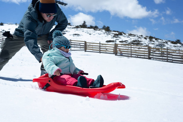 Father pushing a red sled with his little girl on it. Father and his toddler enjoying snow.  - 写真・画像