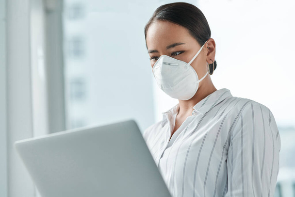 A good connection keeps you going through this crisis. a masked young businesswoman using a laptop in a modern office - Photo, Image