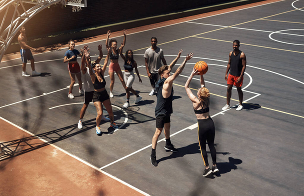 Everyone is totally immersed in the game. a group of sporty young people playing basketball on a sports court - Foto, imagen