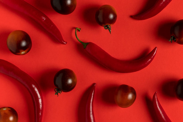 Red hot chili peppers and black strawberry tomatoes on red background. Top view. - Fotó, kép