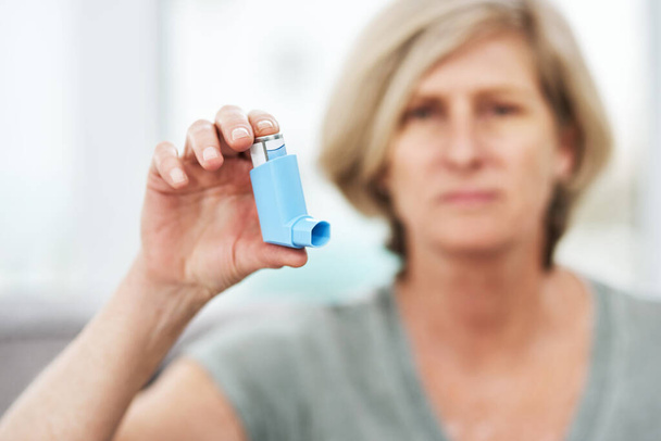 A lifesaver that fits in my pocket. a senior holding an asthma inhaler at home - Foto, immagini