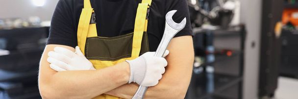 A man in a yellow overalls holds a wrench, close-up. Professional mechanic in garage repairing machinery - Photo, Image