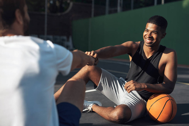 Μπουμ πάει ο δυναμίτης. Ένας αθλητικός νεαρός δίνει στον συμπαίκτη του ένα χτύπημα γροθιάς σε ένα γήπεδο μπάσκετ. - Φωτογραφία, εικόνα