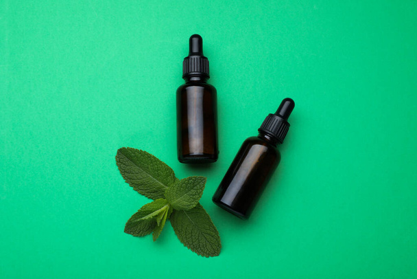 Bottles of essential oil and mint on green background, flat lay - 写真・画像