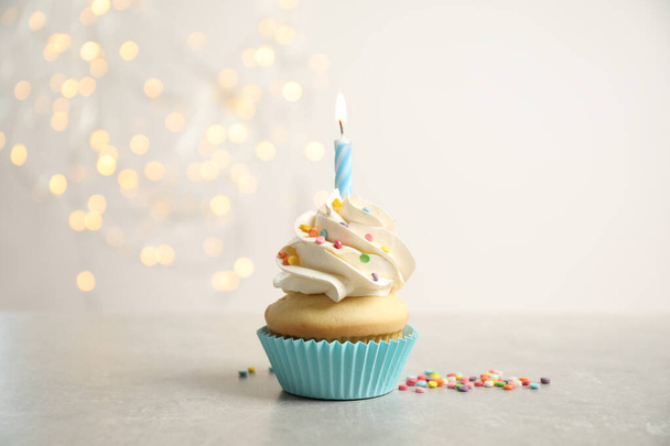 Birthday cupcake with candle on light grey table against blurred lights - Foto, imagen