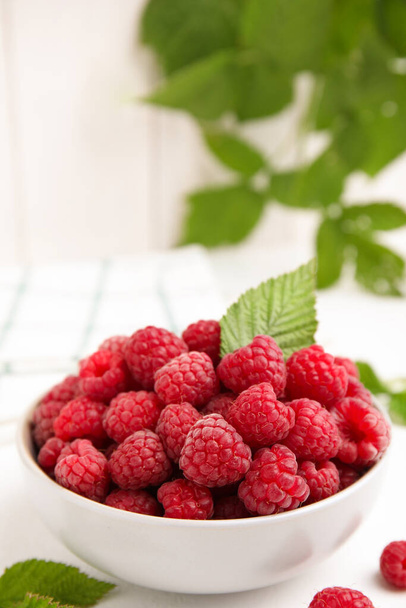 Bowl of fresh ripe raspberries with green leaf on white table, space for text - Photo, image