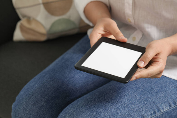 Young woman using e-book reader on sofa, closeup. Space for text - Foto, imagen