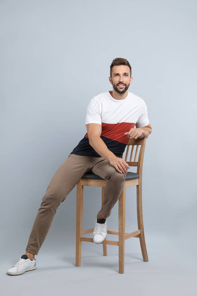 Handsome man sitting on stool against light grey background - Foto, Imagen