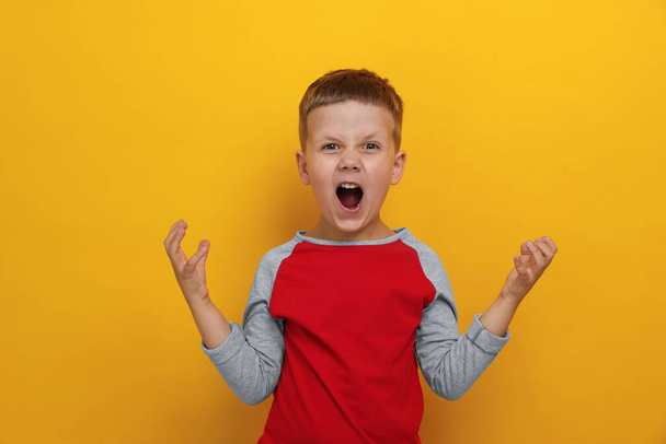 Angry little boy screaming on yellow background. Aggressive behavior - Fotografie, Obrázek