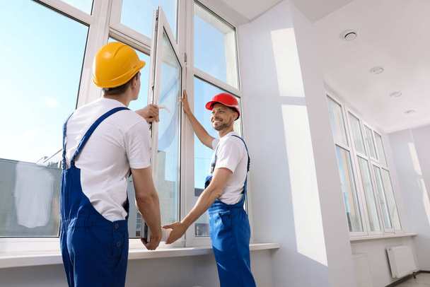 Workers in uniform installing plastic window indoors - 写真・画像