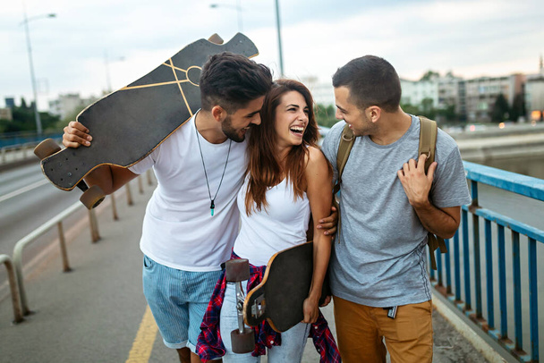 Group of happy friends hang out together and enjoying skateboard outdoors. - Photo, image