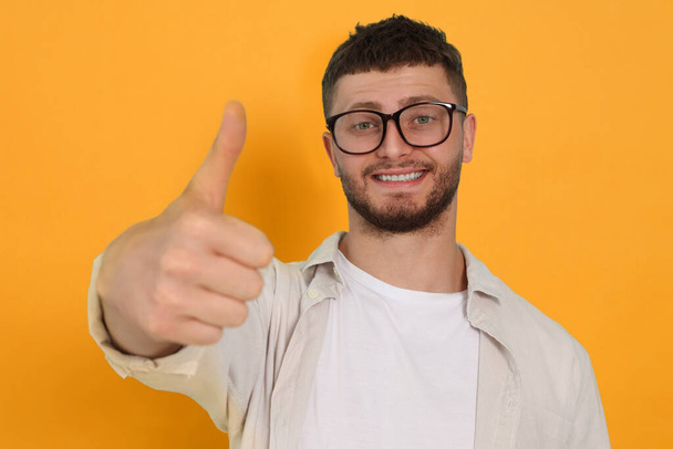 Young man showing thumbs up on orange background - Zdjęcie, obraz