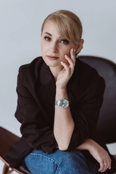 Happy relaxed confident young business woman wearing a suit sitting in a business chair and looking at the camera with a warm friendly smile. Soft selective focus. - 写真・画像