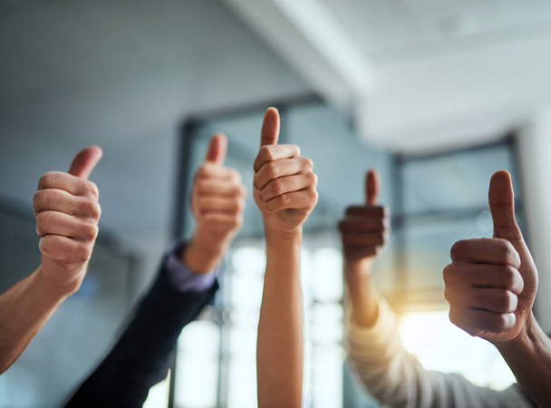 Closeup of business people showing thumbs up hand sign in a modern office. Diverse group of colleagues show positive emoji in support of success. Crowd of employees celebrate team performance - 写真・画像