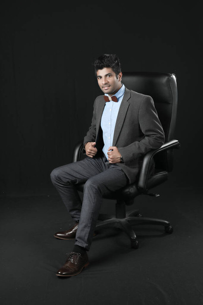 πορτρέτο του νεαρού επιχειρηματία που κάθεται σε μια καρέκλα. Κοιτάζω την κάμερα. απομονωμένο σε μαύρο φόντο - Φωτογραφία, εικόνα