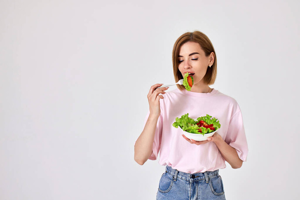 attractive caucasian girl eating fresh vegetable salad on white background. space for text - Fotó, kép