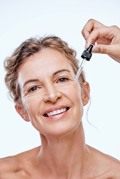 A face serum might be the answer. a mature woman posing with a serum dropper against her face - Foto, immagini