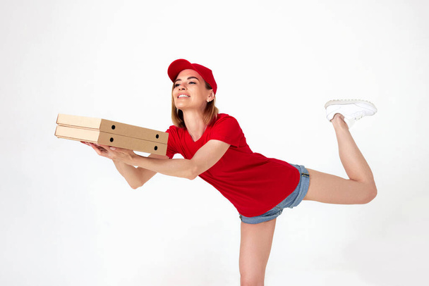 pizza delivery woman in uniform runs in a jump flight holds boxes with pizza on white background. Fast home pizza delivery. - 写真・画像