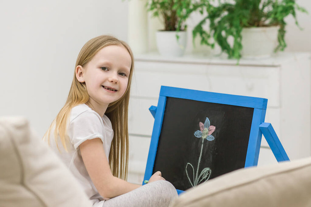 Photo of blonde girl drawing a flower on the white board. Concept of kid girl hobby. - Foto, afbeelding