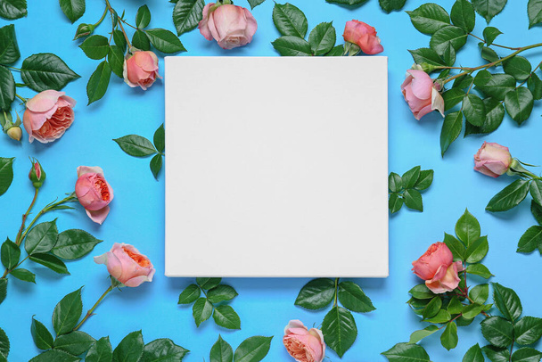 Blank canvas and beautiful pink roses on light blue background, flat lay. Space for design - Fotoğraf, Görsel