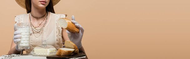 Cropped view of woman in gloves holding milk and bread near butter isolated on beige, banner  - Fotoğraf, Görsel