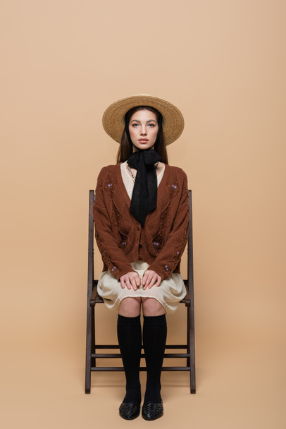 Trendy woman in sun hat sitting on chair on beige background  - Foto, immagini