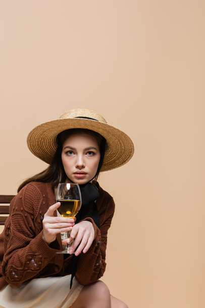 Trendy woman holding glass of wine and looking at camera isolated on beige  - Photo, image