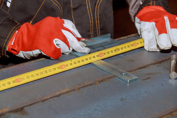 worker measures markings on a metal surface for drilling holes. The worker measures the required distance on the iron surface using a meter. - Fotoğraf, Görsel