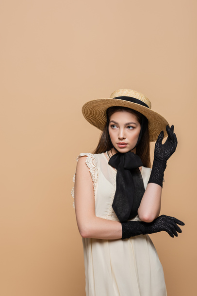 Pretty woman in straw hat and black gloves posing isolated on beige  - Zdjęcie, obraz