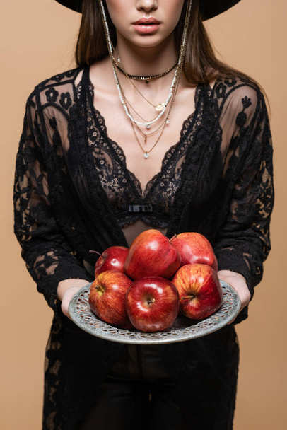 Cropped view of fashionable woman in guipure robe holding ripe apples on plate isolated on beige  - Valokuva, kuva