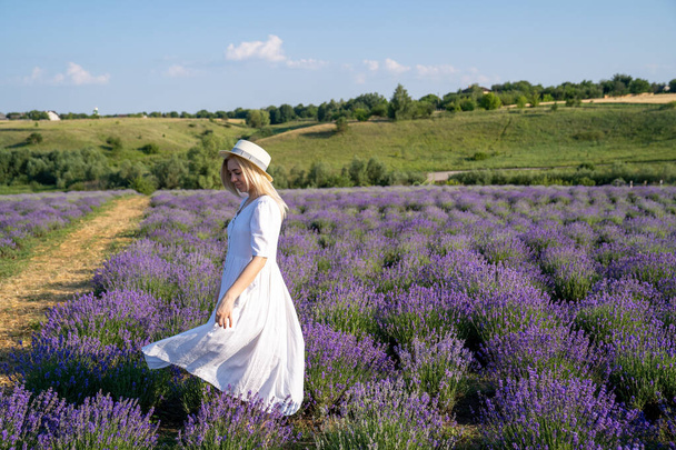 woman model in white dress outfit with hat is standing dancing in lavender field, photo session. Concept of freedom. Good picture for cover, calendar, postcard, wallpaper, background, product, website, blog, business, magazine, shop and store - Фото, изображение