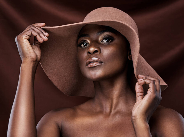 Your skin is your best accessory, take care of it. a beautiful young woman wearing a hat while posing against a brown background - Photo, image
