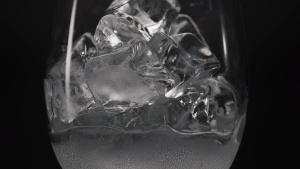 Blocchi congelati fusione vetro da vino primo piano. Cubi di ghiaccio che riempiono vetro trasparente caduto con condensa. Bevande fredde e cocktail macro sfondo nero. Concetto di dissetante - Filmati, video