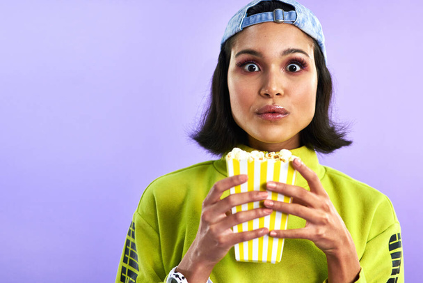 The best movies make you forget about your snacks. Studio shot of a beautiful young woman eating popcorn against a purple background - Valokuva, kuva
