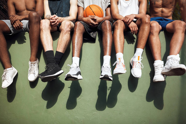 Weekends are for hanging out with basketball buddies. Closeup shot of a group of sporty young men sitting on a wall on a sports court - 写真・画像