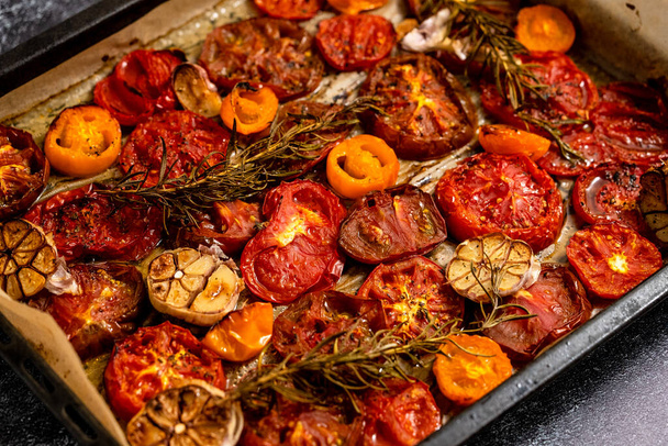 Various kinds of roasted red and yellow tomatoes with thyme and garlic on an metal oven tray. Top view, flat lay - 写真・画像
