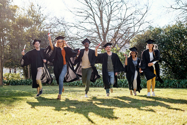 And so a new adventure begins. Portrait of a group of students running together in a row on graduation day - 写真・画像