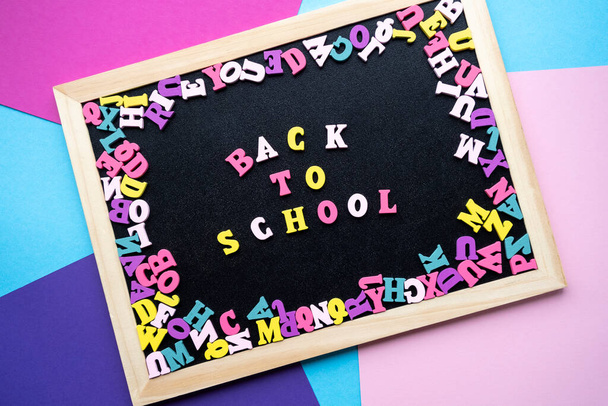 Back to school. Inscription from colored wooden letters on chalkboard. Colorful pink, blue, purple paper background. Copy space, top view. - Foto, Bild