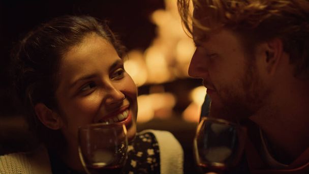 Closeup cheerful couple drink wine on date. Husband wife smiling relax by fireplace. Smiling lovers enjoy romantic honeymoon celebration. Laughing sweethearts talk on holiday. Happiness love concept. - Photo, Image